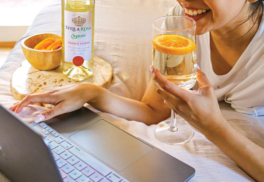 a girl drinking a glass of stella rosa organic orange fusion while browsing on a laptop, signing up for the Sweet Wine Club newsletter