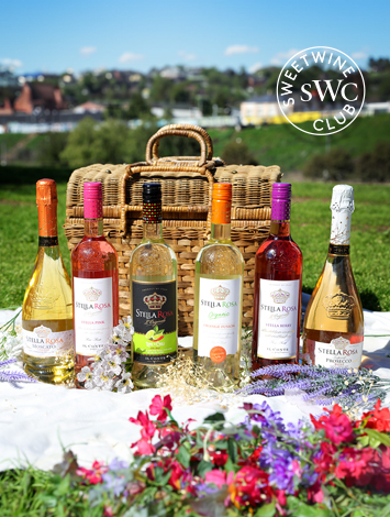 Assortment of Stella Rosa wine bottles in front of a picnic basket on a grassy field, with the Sweet Wine Club logo